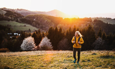 Front view of senior woman hiker walking outdoors in nature at sunset.