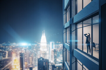 Young businesswoman standing in modern office and looking on night panoramic city.