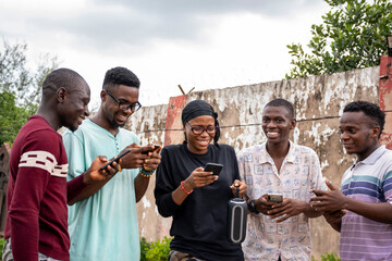 a group of young africans using their phones, hanging out together, students leisure on campus, laughing and having a good time