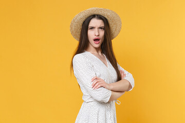 Side view of shocked worried young brunette woman girl in white dress hat posing isolated on yellow background. People lifestyle concept. Mock up copy space. Holding hands crossed, looking camera.