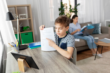 children, education and school concept - student boy with tablet pc computer and test learning online at home