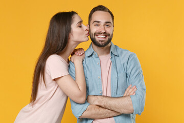 Smiling young couple two friends guy girl in pastel blue casual clothes posing isolated on yellow background. People lifestyle concept. Mock up copy space. Holding hands crossed, kissing in cheek.