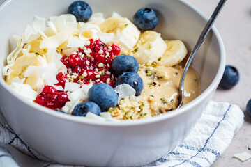 Oatmeal bowl with banana, berries, hemp seeds and coconut slices. Healthy vegan breakfast concept.