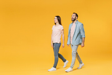 Cheerful young couple two friends guy girl in pastel blue casual clothes posing isolated on yellow background studio portrait. People lifestyle concept. Mock up copy space. Walking, looking aside.