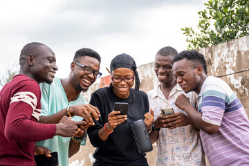 group of young african students using their phones, hanging out together, leisure on campus, viewing content on a phone together, laughing