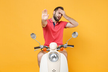 Tired young bearded guy in summer clothes driving moped isolated on yellow background. Driving motorbike transportation concept. Mock up copy space. Showing stop gesture with palm, put hand on head.
