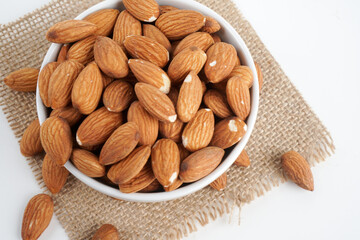 almonds in white bowl and glass of milk and brown fabric on white background. top view and flat lay, 