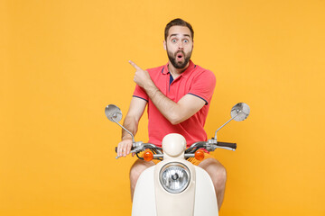 Shocked young bearded man guy in casual summer clothes driving moped isolated on yellow background studio. Driving motorbike transportation concept. Mock up copy space. Pointing index finger aside up.