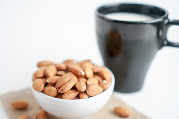 almonds in white bowl and glass of milk and brown fabric on white background. top view and flat lay, 