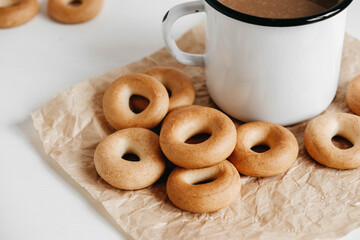 Metal mug with hot drink and mini round bagels on a white wooden background. Copy, empty space for text