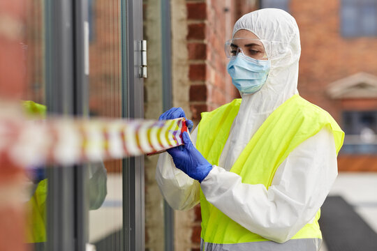 quarantine and pandemic concept - healthcare worker in protective gear or hazmat suit, medical mask, gloves and goggles enclosing building with caution tape outdoors