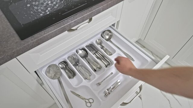 Male hand picks some table kives from kitchen drawer