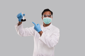 Fototapeta na wymiar Male Doctor Pointing at Flask with Colorfull Liquid Wearing Medical Mask, Gloves and Glasses Isolated. Science, Medical, Virus Concept. Indian Man Doctor Smilling.