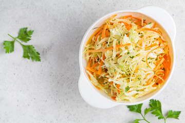 Fresh coleslaw salad with cabbage and carrots in white bowl, top view.