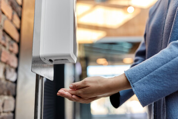 hygiene, health care and safety concept - close up of woman using hand sanitizer from dispenser at...