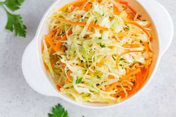 Fresh coleslaw salad with cabbage and carrots in white bowl, top view.