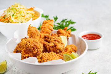 Crispy fried chicken in a white bowl with cole slaw salad and sauce.