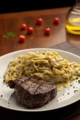 steak with pasta tagliatelle fetuccini on plate with blurred background with tomatoes olive oil and wine glass