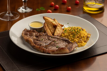 steak and fries with sauce on plate with blurred background with tomatoes olive oil and wine glass