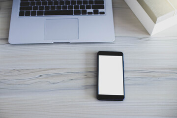 Close up mobile phone on a white background with laptop on wooden desk, selective focus.