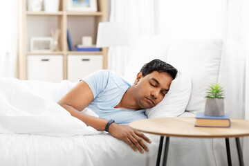 people, bedtime and rest concept - indian man with health tracker sleeping in bed at home