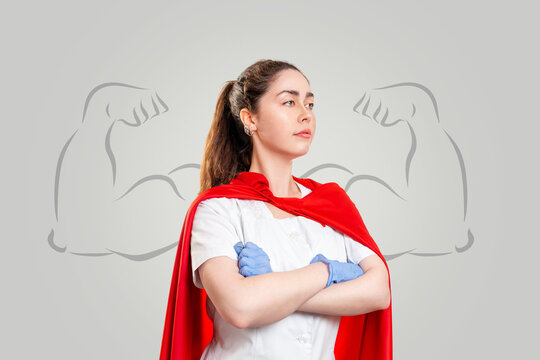 A doctor in surgical gloves and a red superhero Cape, posing against a background of painted strong hands on a gray background. Super hero power for clinic and hospital personal