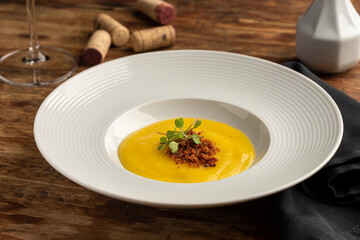 carrot, parsnip, pumpkin cream with bacon on white plate wooden table