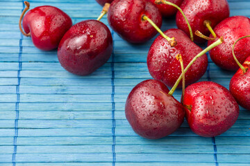 Top view of wet cherries on blue wooden tablecloth, selective focus, horizontal, with copy space