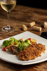 fish baked with crust and vegetables on white plate on a wooden table