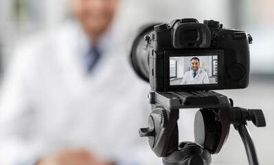 healthcare, medicine and blogging concept - happy smiling male doctor with camera recording video blog at hospital