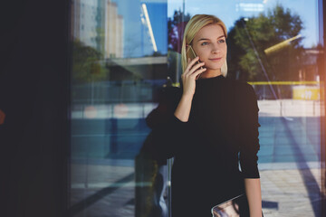 Portrait of beautiful young female holding mobile phone in hands while strolling urban park.