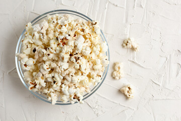popcorn in a transparent glass bowl on white table with few popcorn beside bowl.