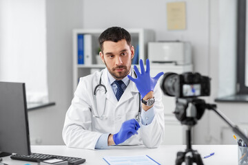 Fototapeta na wymiar healthcare, medicine and blogging concept - male doctor with camera and gloves recording video blog at hospital