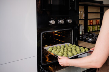Woman hands put in the oven raw falafel arranged on baking paper in the tray. Healthy food diet, vegan background