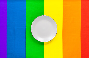 White plate on a rainbow flag LGBT flag of six colors for design. Design of the dining table for the LGBT community. Rainbow tablecloth for lunch.