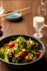 Green salad with lettuce arugula tomatoes on a ceramic bowl and dressing on cup