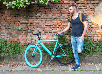 fashionable man portrayed next to his beautiful minimal bicycle, background of red and solid brick wall, fashionable and ecological urban transport concept