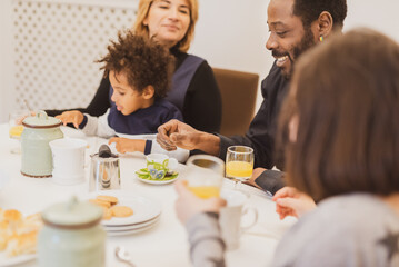 Fototapeta na wymiar Happy interracial family with little children having breakfast in the morning, moments of daily life with Caucasian mother, African father and mixed-race children, vintage filter