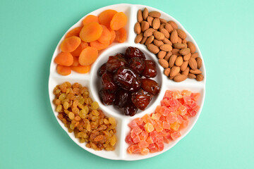 Mix of dried fruits and nuts on a white plate. Apricot, almond, raisin, dates fruit. On a green background. Space for text or design.