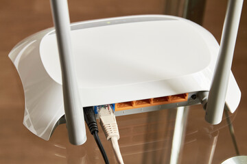 White wireless router on a glass table connected by cable to the Internet. Close-up
