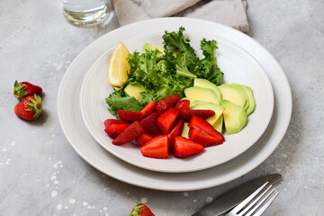keto avocado salad with strawberry and lettuce leaves, a glass of water with lemon. food healthy breakfast or lunch. salad in a white bowl, top view.