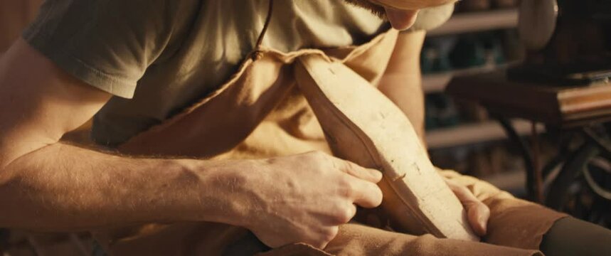 Traditional bespoke shoemaker cut shape leather insole on wooden shoe last with knife in small business reopen workshop