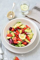 keto avocado salad with strawberry and lettuce leaves, a glass of water with lemon. food healthy breakfast or lunch. salad in a white bowl, top view.