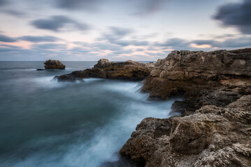Fototapeta na wymiar Amazing long exposure seascape with rocky beach and stormy sea at sunrise in the blue hour