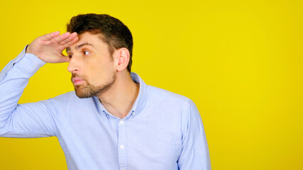 Handsome bearded man looks away with his hand to his forehead on a yellow background with copyspace. Guy in a light blue shirt. Place for text or product