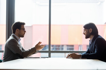 Side view two businessmen talking at negotiations solve current issues, sales manager make offer to...