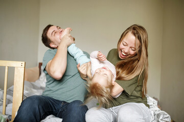 Young happy parents playing with their toddler funny joyful girl