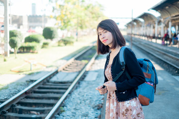 Asian woman tourists is standing on a backpack. Wait for the train to travel. On vacation.