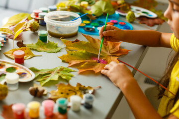 Little girl painting on autumn yellow leaves with gouache, kids arts, children creativity, autumn art.