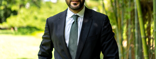 close up to Arabian business man with his suit and tie, stands in the outdoor green garden field at the afternoon.